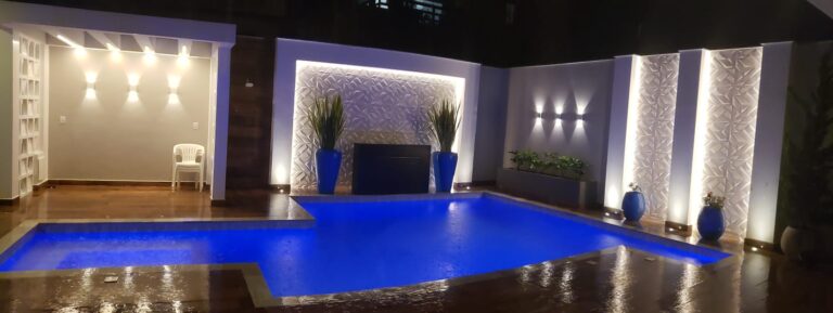 Piscina coberta e climatizada com iluminação em LED azul e parede decorativa, projeto da Ramiro Piscinas