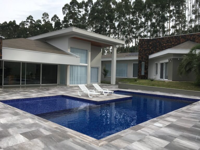 Piscina em tom escuro integrada à arquitetura de residência contemporânea, projeto da Ramiro Piscinas